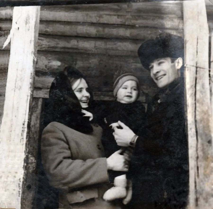 Чёрно-белая фотография: молодая пара с ребёнком на руках у бревенчатого дома